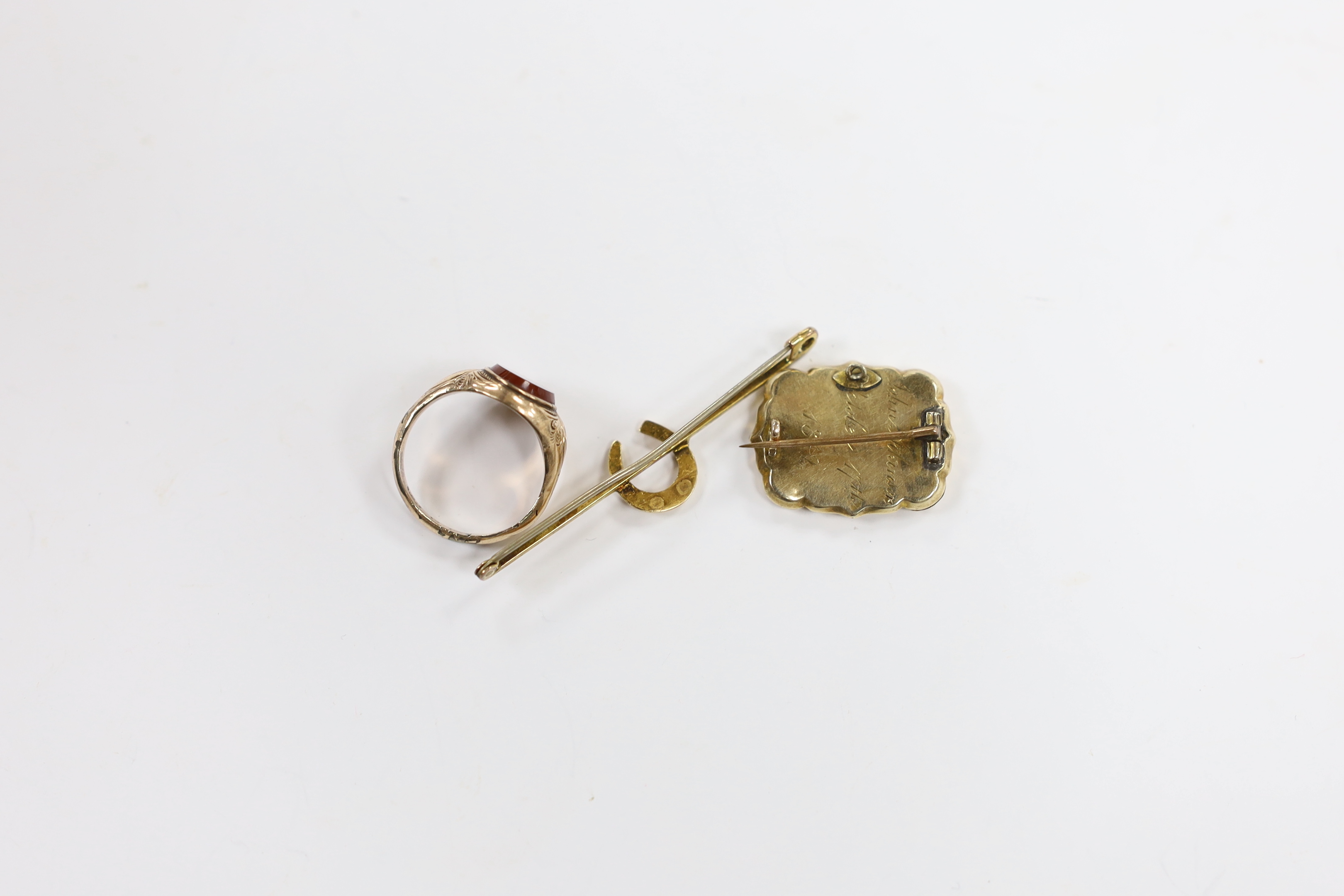 A Victorian 9ct and carnelian set signet ring, size L, an early Victorian yellow metal and plaited hair set mourning brooch, dated 1842 and a 9ct horseshoe bar brooch.